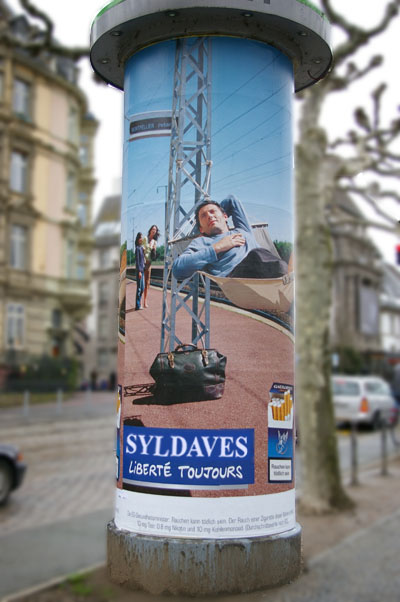 Frappafort, Bordurie, publicité de rue représentant un homme dans un hamac, une broumpfette à la main. Le slogan lit "Syldaves, liberté toujours"